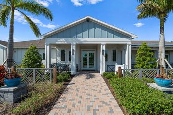 the front of a house with a walkway and palm trees